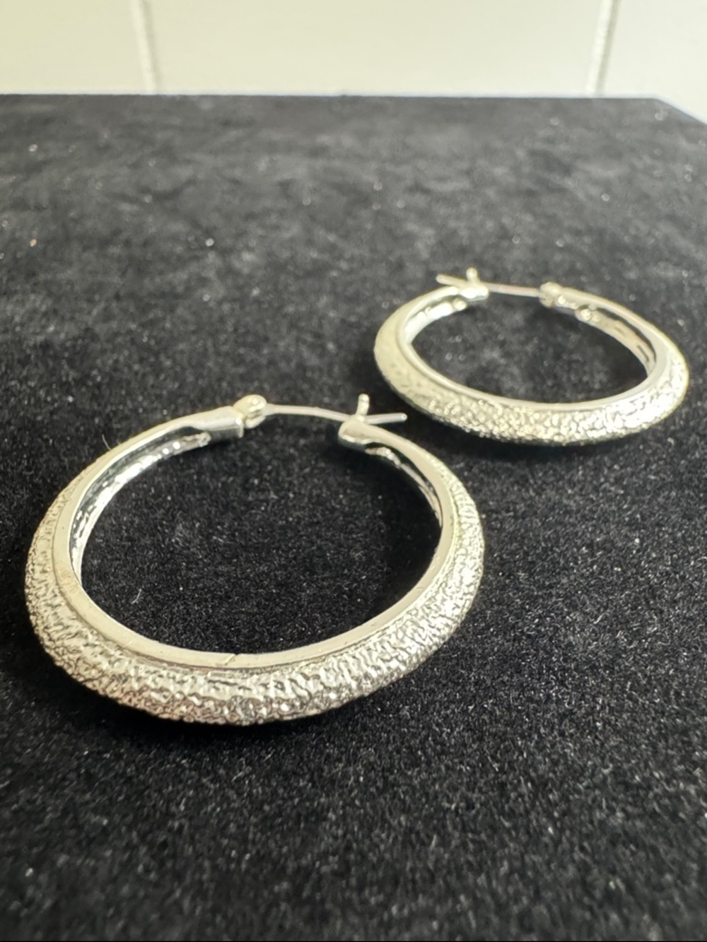 Silver-toned hoop earrings with textured sparkle finish surface.